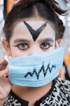 Close up Vertical shot of Kid in Halloween witch dress and scary face removing medical mask by looking into camera.