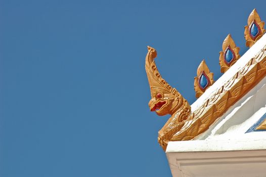 Thai traditional naga decoration on temple roof under blue sky