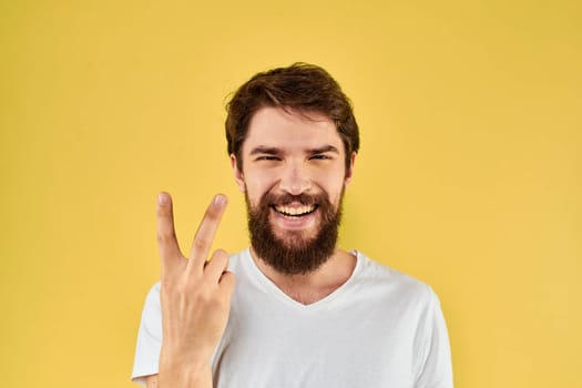 Bearded man emotions fun gesture with hands white t-shirt close-up yellow background. High quality photo