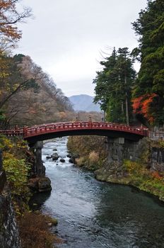 Ancient Japanese red arc bridge crossing creek surrounded by Autumn leaves in Senda Japan