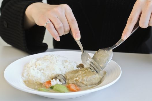 A lady eating curry rice with spoon and fork