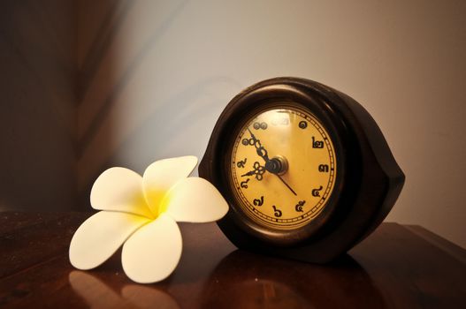 Vintage wooden Thai desk clock on a table with plumeria flower