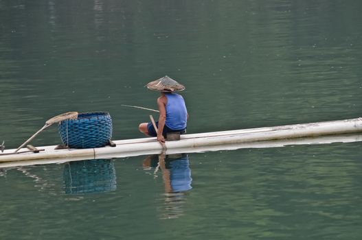 Chinese fisherman on bamboo raft uses traditional method to catch fish in Guilin river