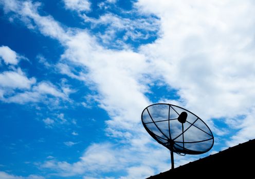 Black satellite TV receiver plate on the roof with a blue sky background.