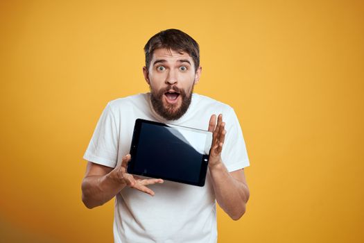 Man with a tablet on a yellow background in a white t-shirt new technologies businessman touch screen touchpad. High quality photo