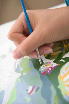 2 - Vertical image of youthful hand painting by numbers with a bright blue brush. Bright image, with clean whites. Green and blue colors strong.