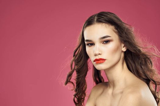 Beautiful brunette woman with makeup on her face on a pink background naked shoulders. High quality photo