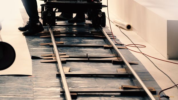 Behind the scenes of production team setting dolly track for video camera equipment before movie shooting in a big studio. 