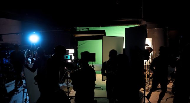 Behind the scenes or the making of film video production and movie crew team working in silhouette of camera and equipment set in studio. 
