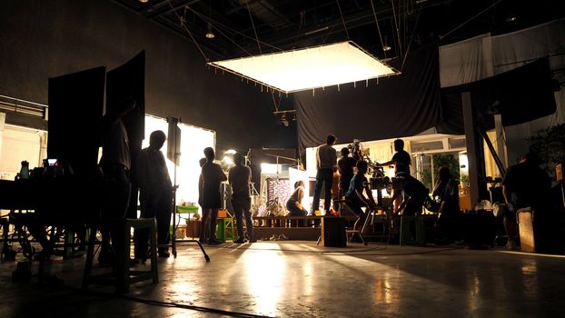 Behind the scenes or the making of film video production and movie crew team working in silhouette of camera and equipment set in studio. 