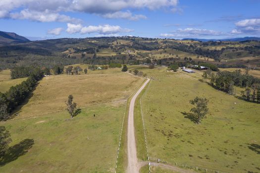 Aerial view of a dirt road with white fence post markers in a green agricultural field