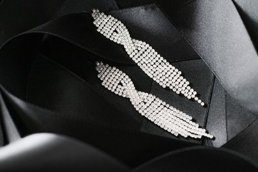 Luxury diamond earrings on black silk ribbon as background, jewelry and fashion brands