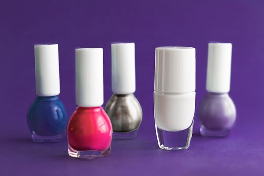 Nail polish bottles on dark purple background, beauty branding