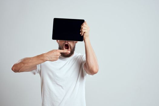 emotional man with a tablet in front of his eyes gesturing with his hands cropped view Copy Space Model light background. High quality photo