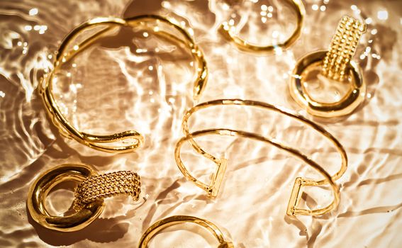 Jewellery branding, fashion gift and luxe shopping concept - Golden bracelets, earrings, rings, jewelery on gold water background, luxury glamour and holiday beauty design for jewelry brand ads