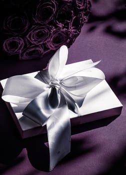 Happy holidays, luxe shopping and love gifts concept - Luxury holiday silk gift box and bouquet of roses on purple background, romantic surprise and flowers as birthday or Valentines Day present