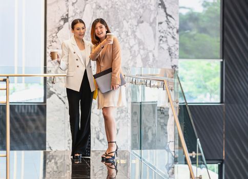 Two asian businesswomen walking and talking during coffee break in modern office or coworking space, coffee break, relaxing and talking after working time, business and people partnership concept