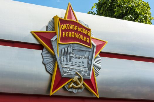 Minsk, Belarus - may 27, 2017: Plaster bas-relief of the order of the October revolution closeup on blue sky background and tree with the words "October revolution"