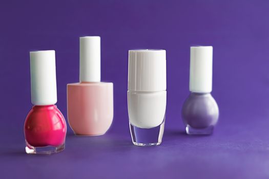 Nail polish bottles on dark purple background, beauty branding