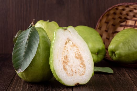 Close up of delicious beautiful guava set with fresh green leaves isolated on dark wooden table background.