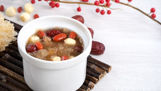 Close up of traditional Chinese sweet snow white fungus soup with lotus seed, red dates (jujube) and wolfberry (goji, gojiberry) on white background.