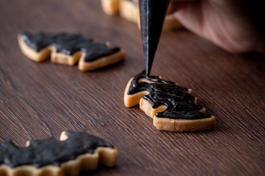 Close up of decorating cute Halloween bat gingerbread sugar cookies with frosting icing cream topping bag.