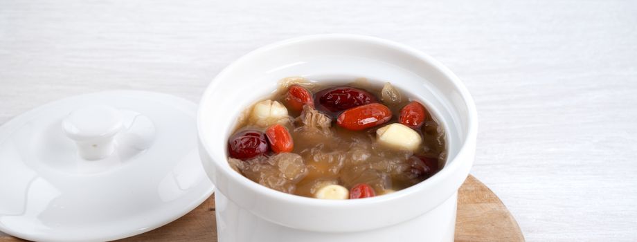 Close up of traditional Chinese sweet snow white fungus soup with lotus seed, red dates (jujube) and wolfberry (goji, gojiberry) on white background.