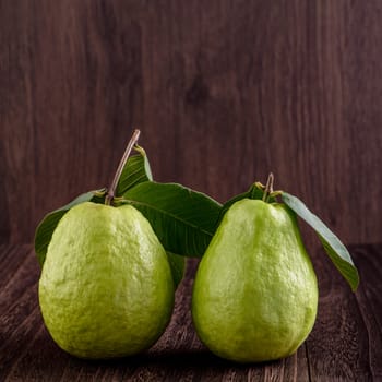Close up of delicious beautiful guava set with fresh green leaves isolated on dark wooden table background.