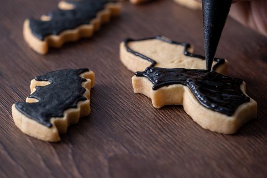 Close up of decorating cute Halloween bat gingerbread sugar cookies with frosting icing cream topping bag.