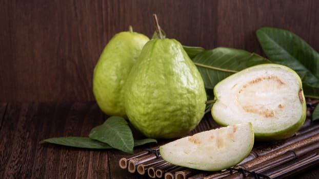 Close up of delicious beautiful guava set with fresh green leaves isolated on dark wooden table background.