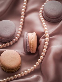 Girly, bakery and branding concept - Sweet macaroons and pearls jewellery on silk background, parisian chic jewelry, French dessert food and cake macaron for luxury confectionery brand, holiday gift