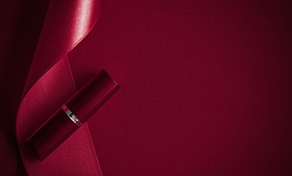 Cosmetic branding, glamour lip gloss and shopping sale concept - Luxury lipstick and silk ribbon on maroon holiday background, make-up and cosmetics flatlay for beauty brand product design