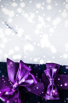 Branding, glamour and cold season concept - Winter holiday gift box with purple silk bow, snow glitter on marble background as Christmas and New Years presents for luxury beauty brand, flatlay design