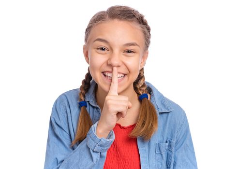Happy teenage girl keeps fore finger on lips, asking for silence, isolated on white background