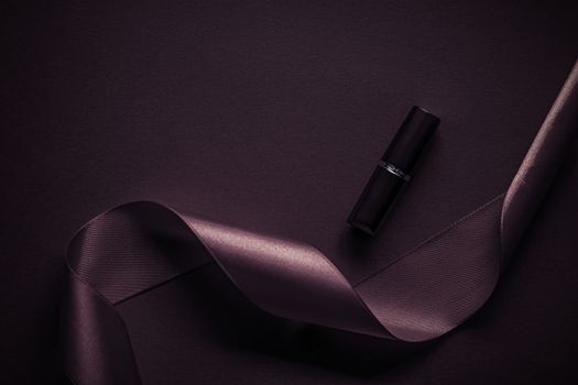 Cosmetic branding, glamour lip gloss and shopping sale concept - Luxury lipstick and silk ribbon on dark purple holiday background, make-up and cosmetics flatlay for beauty brand product design