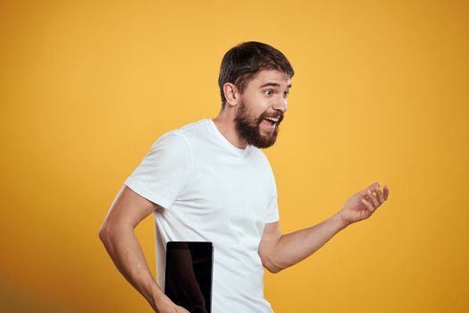 Man with a tablet on a yellow background in a white t-shirt new technologies businessman touch screen touchpad. High quality photo