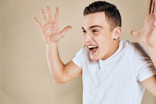 Emotional man white t-shirt gestures with hands lifestyle beige background. High quality photo