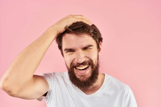 Bearded man in white t-shirt gesturing with hands facial expression close up pink background. High quality photo