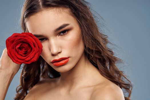 Portrait of a woman with a red rose in her hands on a gray background naked shoulders evening makeup. High quality photo