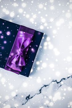 Branding, glamour and cold season concept - Winter holiday gift box with purple silk bow, snow glitter on marble background as Christmas and New Years presents for luxury beauty brand, flatlay design