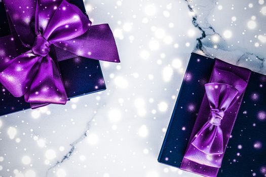 Branding, glamour and cold season concept - Winter holiday gift box with purple silk bow, snow glitter on marble background as Christmas and New Years presents for luxury beauty brand, flatlay design