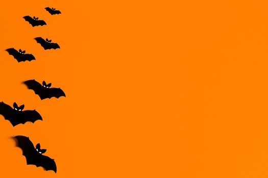 orange background with a flock of black paper bats for Halloween, black paper bat silhouettes on an orange background, Halloween concept, copyspace, flatlay, top view, overhead.