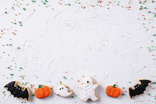 Top view of Halloween festive decorated icing gingerbread sugar cookies on white background with copy space and flat lay layout.