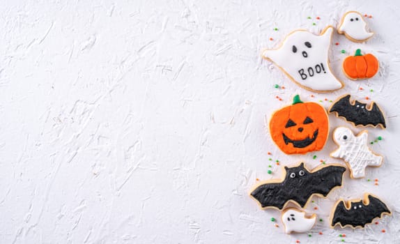 Top view of Halloween festive decorated icing gingerbread sugar cookies on white background with copy space and flat lay layout.