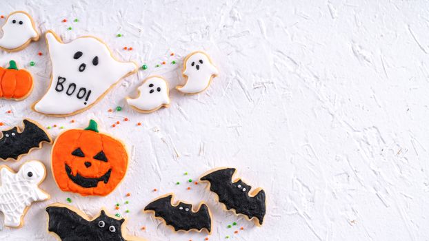 Top view of Halloween festive decorated icing gingerbread sugar cookies on white background with copy space and flat lay layout.