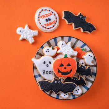 Top view of Halloween festive decorated icing gingerbread sugar cookies on orange background with copy space and flat lay layout.