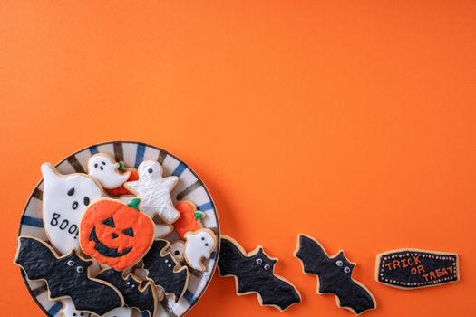 Top view of Halloween festive decorated icing gingerbread sugar cookies on orange background with copy space and flat lay layout.