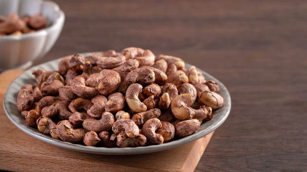 Cashew nuts with peel in a plate on wooden tray and table background, healthy raw food concept.