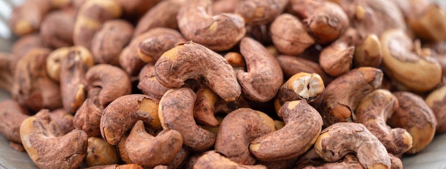 Cashew nuts with peel in a plate on wooden tray and table background, healthy raw food concept.