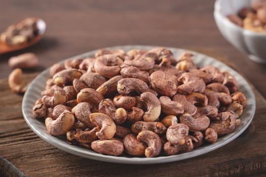 Cashew nuts with peel in a plate on wooden tray and table background, healthy raw food concept.